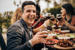 © Lomb - Smiling man enjoying outdoor dinner with friends during a cheerful wine toast