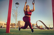 © Lomb - Focused female athlete performing lunges with suspension straps in urban park