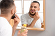 © Pixel-Shot - Handsome young happy man cleansing his face with micellar water and cotton pad near mirror in bathroom