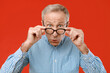 © Prostock-studio - A man adjusts his glasses and shows a surprised expression while standing in front of a red background. He wears a checkered shirt and has gray hair. The scene has good lighting.