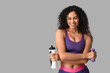 © Pixel-Shot - Sporty young African-American female coach with water bottle and dumbbells on white background
