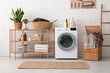 © Pixel-Shot - Modern washing machine, shelving unit, basket with laundry and ladder in room