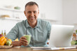 © Pixel-Shot - Mature man with glass of fresh vegetable smoothie using laptop in kitchen