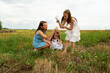 © Mariia - Mother and girls picking daisies in a field on a summer day