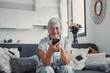 © Daniel - Elderly woman sits on a sofa at home using her smartphone to browse and shop online. She focuses on digital communication and enjoys a modern e-commerce lifestyle.