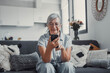 © Daniel - Elderly woman sits on a sofa at home using her smartphone to browse and shop online. She focuses on digital communication and enjoys a modern e-commerce lifestyle.