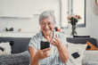 © Daniel - Elderly woman sits on a sofa at home smiling during a video call with family and friends. She enjoys connecting with loved ones and sharing cheerful moments in a modern digital lifestyle.