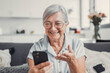 © Daniel - Elderly woman sits on a sofa at home smiling during a video call with family and friends. She enjoys connecting with loved ones and sharing cheerful moments in a modern digital lifestyle.