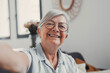 © Daniel - Elderly woman takes a selfie on a sofa at home, smiling and feeling cheerful. She enjoys a calm and peaceful moment while sharing her life on social media in a reflective way.