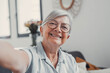 © Daniel - Elderly woman takes a selfie on a sofa at home, smiling and feeling cheerful. She enjoys a calm and peaceful moment while sharing her life on social media in a reflective way.