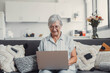 © Daniel - Elderly woman sits on a sofa at home using her computer to browse and shop online. She focuses on digital communication and enjoys a productive e-commerce routine.