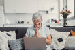 © Daniel - Elderly woman sits on a sofa at home smiling during a video call with family and friends. She enjoys connecting and sharing happy moments through modern technology.