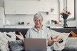 © Daniel - Elderly woman sits on a sofa at home smiling during a video call with family and friends. She enjoys connecting and sharing happy moments through modern technology.