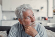© Daniel - Senior man sits alone on a sofa looking outside with a sad expression. He seems stressed and reflective while dealing with personal concerns at home.