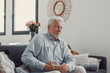 © Daniel - Elderly man sits on a sofa holding his stomach in pain. He struggles with abdominal discomfort and fatigue while trying to relax at home.