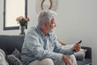 © Daniel - Senior man sits on a sofa smiling while using his smartphone. He enjoys browsing, buying, and connecting with the digital world at home.