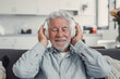 © Daniel - Elderly man sits on a sofa at home enjoying music with headphones. He feels relaxed, happy, and carefree while immersing himself in sound and leisure.