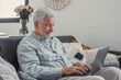 © Daniel - Elderly man sits on a sofa using his computer to browse and shop online. He enjoys a productive lifestyle while staying connected digitally at home.