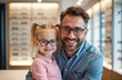 © miss irine - Smiling father and daughter try on eyeglasses in optical store. They examine frames choosing new vision correction eyewear. Family selects glasses for better sight.