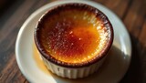 Close up on creamy creme brulee dessert. Caramelized sugar crust on top with liquid caramel dripping slightly. Served in white ramekin dish on wooden table.