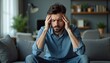 © miss irine - Young man sits on couch, clutches head, looking stressed and worried. He has problems, feels pain and anxiety. Needs help with mental health issues, work pressure or life crisis.