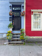 © Dolores  Harvey - A blue house with a black door. There's a small window in the door, and over called a transom window. The adjoining house is vibrant red with white trim. The steps to the door have colorful flowerpots
