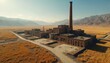 © Vadym - Vast abandoned brick factory with tall smokestack in dry grassy field. Crumbling industrial site lies in remote valley near arid mountains under clear sky.