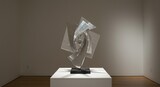 Metal sculpture on a white pedestal in a gallery geometric shapes silver color against a plain wall