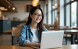 © zhao - Pretty cheerful Asian woman in eyeglasses and casual clothes browses laptop computer connected to 4g internet updates software uses modern technologies poses in cafeteria looks gladfully away