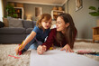 © Stockphotodirectors - A woman and a young child engage in a fun drawing activity on the floor. They are surrounded by colorful crayons and are enjoying quality time together in a warm, cozy living room.