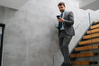 © Novak - Young businessman using smartphone while walking down stairs with laptop.
