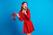 © deagreez - Young chic woman in red polka dot dress smiling while holding a red high heel against a blue background