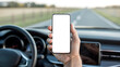 © Atik - Hand holding a smartphone with blank screen inside a car on a road