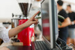 © Crystal - Barista hand pressing touch screen monitor, operating POS system for customer order in a coffee shop. Back view of worker