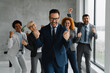 © Novak - A diverse team of successful professionals smiling and making positive hand gestures in a modern office. Concept of victory, great teamwork, and corporate success.
