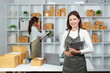 © Natee Meepian - E-commerce workspace. Smiling woman in apron holding tablet in a retail environment.