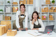 © Natee Meepian - Teamwork in retail. Two women smiling in an e-commerce workspace with packages.
