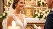 © NeuroCake - A happy bride in a white lace dress smiles at her groom during their church wedding. Couple at the altar during a traditional matrimony ceremony