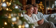 © sam richter - Smiling partners relaxing on sofa browsing smartphone beside glowing festive decorations.