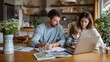 © Olena - Modern family working together at a kitchen table with parents planning on paper and laptop while a young child uses a computer. The image represents remote work, family teamwork