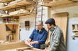 © Robert Kneschke - Experienced craftsman teaching young apprentice in busy lumberyard workshop