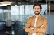 © Liubomir - Smiling bearded man standing in a modern office with arms crossed, projecting confidence, professionalism and success as a young executive or entrepreneur in a corporate setting