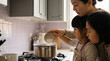 © smth.design - Mother and children cooking together at home kitchen stove, pouring ingredients into steaming pot and learning family meal preparation