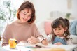 © Hip.hub - Mother and daughter engage in drawing and writing activity indoors during daylight hours in a cozy home setting