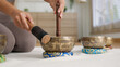 © Leny Studio - Calm sound healing with tibetan singing bowl session soft mat, close hands guide wooden mallet bright home studio, warm light and mindful focus create gentle Sound Healing Tibetan singing bowl