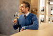 © BGStock72 - Man holds a glass of wine while standing at a bar in a wine shop
