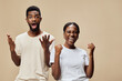 © SHOTPRIME STUDIO - Happy African couple celebrating success with joyful expressions, dressed in casual light clothing, set against a beige background
