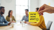 © Visual Verse - Hand holding motivational sticky note at business meeting