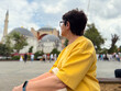 © satura_ - Adult woman sitting in city square looking at historic architectural landmark in Istanbul. Cultural curiosity, tourism reflection, slow travel experience, and personal connection with urban heritage.