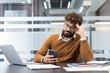 © Liubomir - Young man in glasses sitting at office desk, appearing bored and distracted while using a mobile phone instead of working, feeling unmotivated and delaying tasks